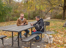 Two 65 year old men sat a park bench with a dog